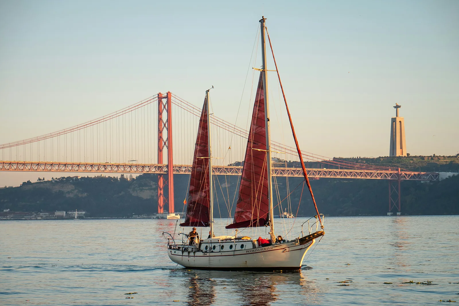 Un velero de velas rojas en el Tajo, con el puente 25 de Abril al fondo